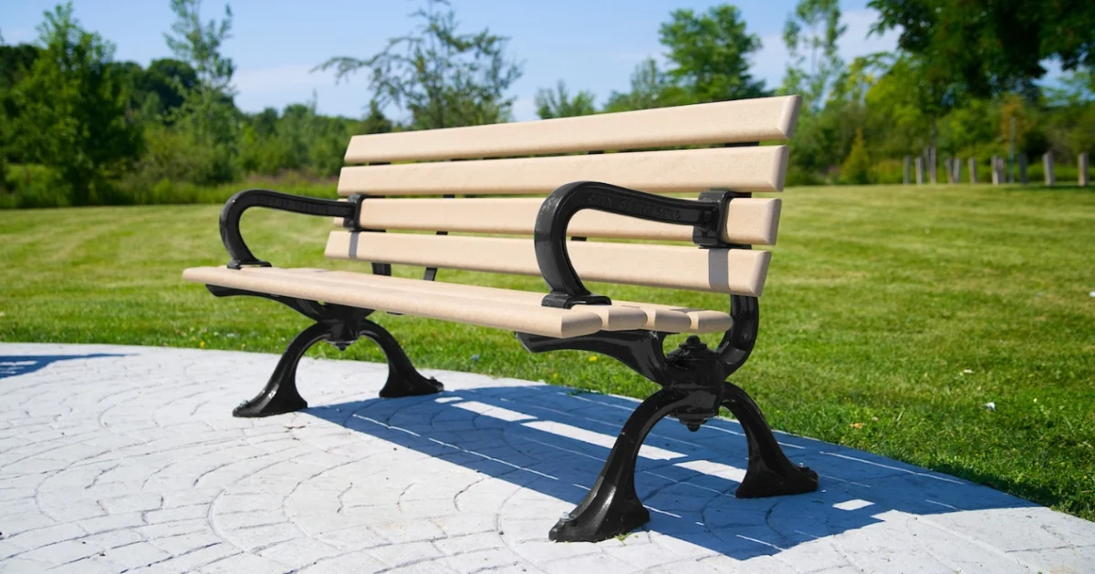 Beige park bench with black frame on decorative concrete platform.